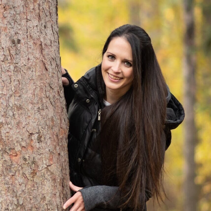 A woman leaning against a tree in the woods.